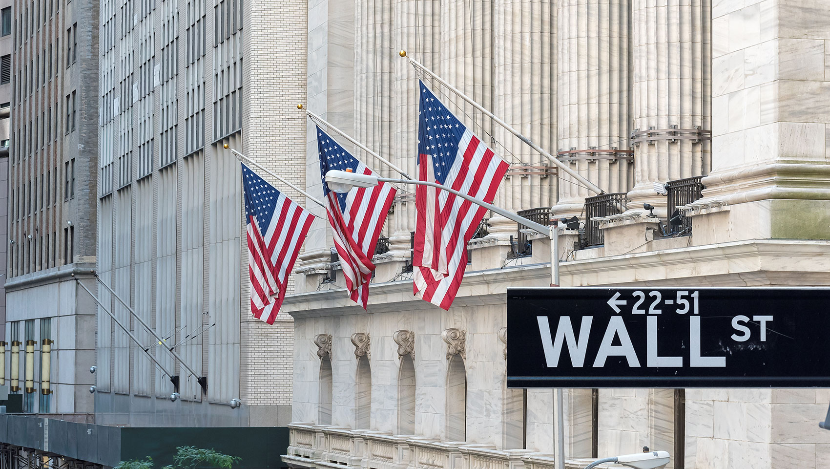 Wall St. Street sign in front of building with American flags